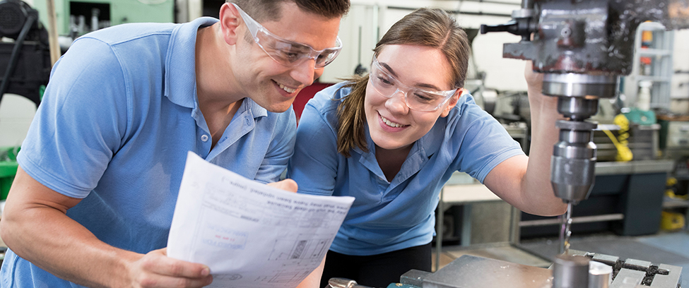Engineer Instructing Female Apprentice On Use Of Drill