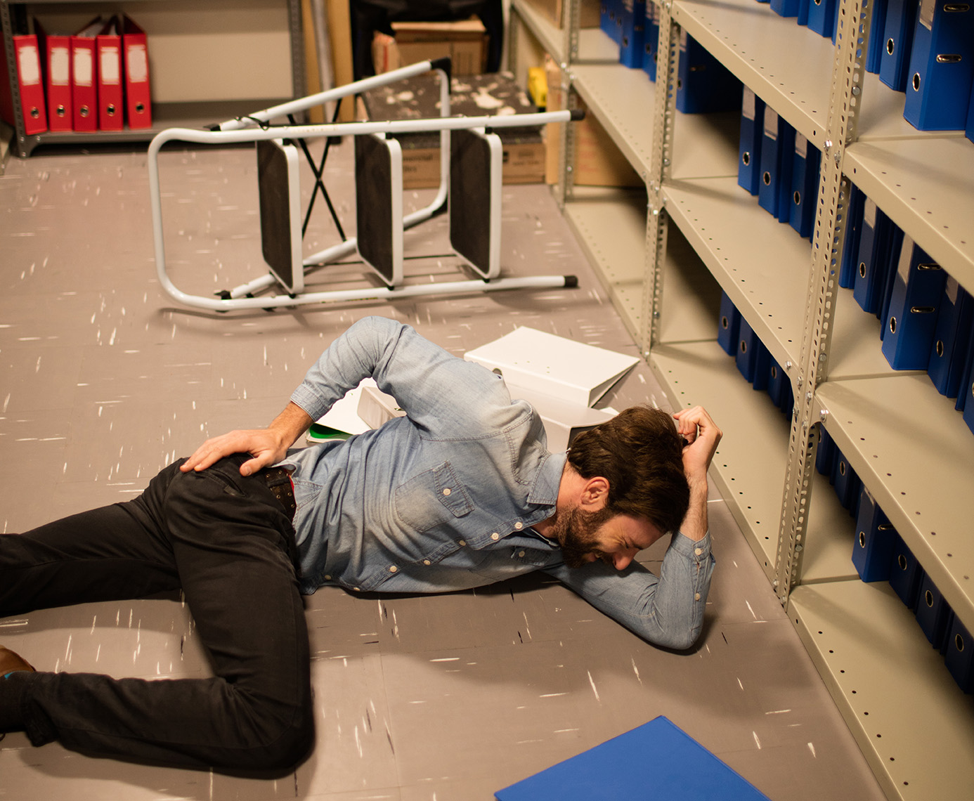 Fallen businessman with file in storage room at workplace