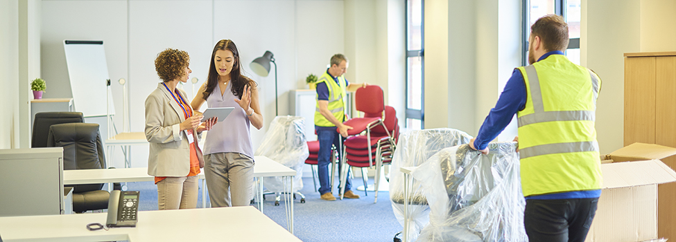 a new business venture is moving into some new offices. The mid adult businesswoman is chatting about layout with her assistant as removal men bring in the office furniture .