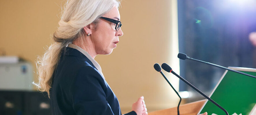 Mature elegant female in suit speaking in microphone at public forum