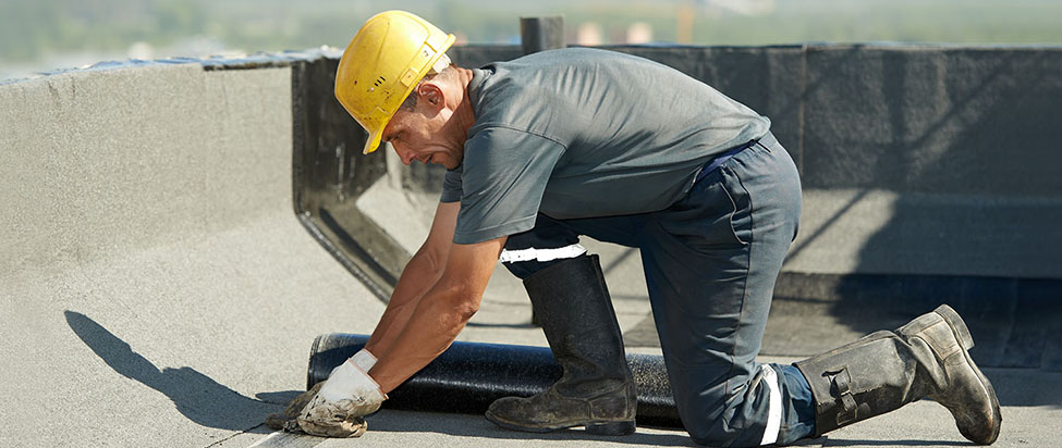 Roofer preparing part of bitumen roofing felt roll for melting by gas heater torch flame