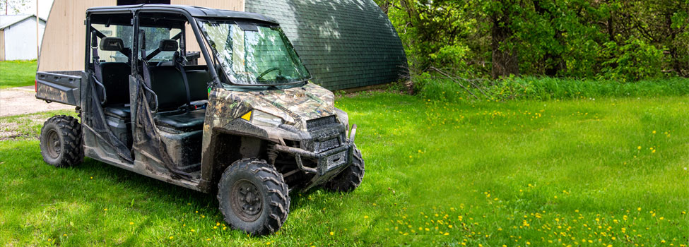 Camouflage colored ATV golf cart parked outside an outbuilding on the grass,
