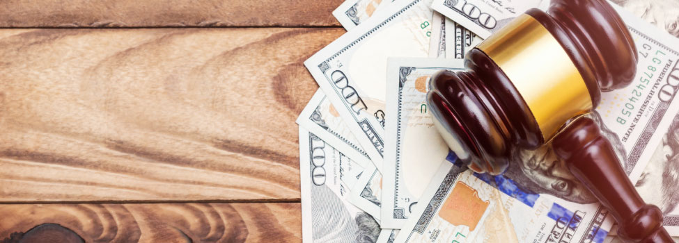 Gavel placed atop of a pile of $100 bills. Wood table background.